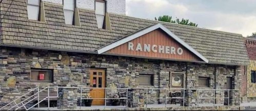 A stone building with a sloped roof and a sign reading "Ranchero" above the entrance.
