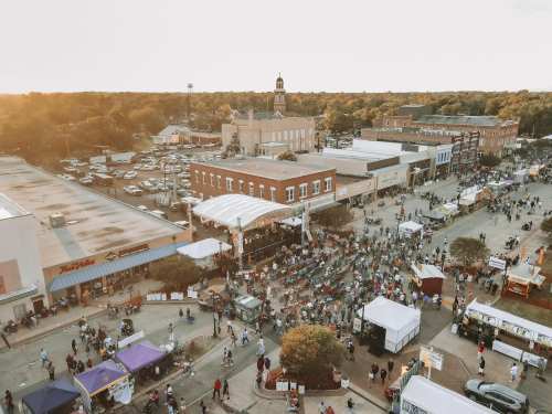 Aerial view of a bustling street festival with crowds, food stalls, and a historic building in the background.