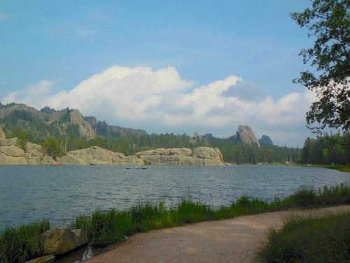 Scenic view of a calm lake surrounded by rocky hills and lush greenery under a partly cloudy sky.