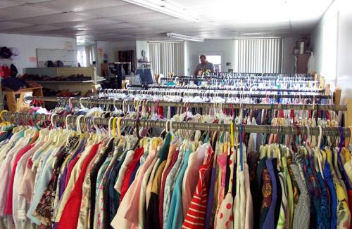 A clothing rack filled with colorful garments in a spacious store, with a person browsing in the background.