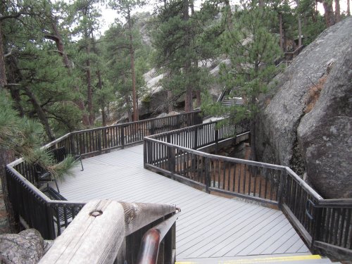 A wooden boardwalk winding through a forested area with rocks and pine trees.