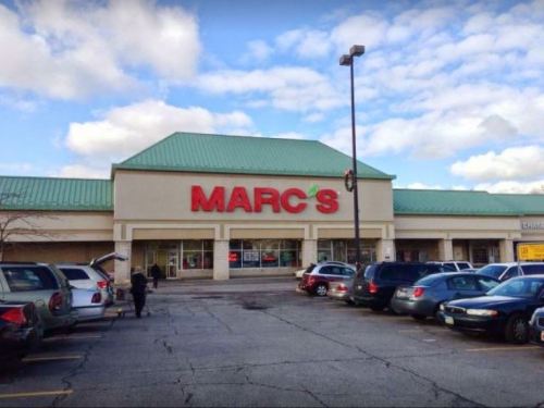 Exterior of a Marc's store with a green roof and large red signage, surrounded by parked cars under a cloudy sky.