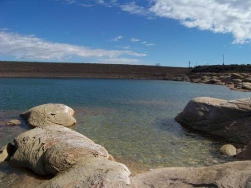 A serene lake with clear water, surrounded by smooth rocks and a blue sky with scattered clouds.