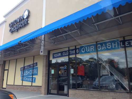 Storefront of "Uptown Cheapskate" with blue awning, signs promoting clothing exchange and cash offers.