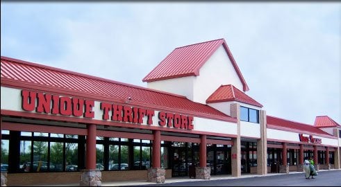 Exterior of a Unique Thrift Store with a red roof and large windows, set against a cloudy sky.