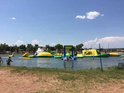 A colorful inflatable water park with slides and obstacles in a lake, surrounded by trees and blue skies.