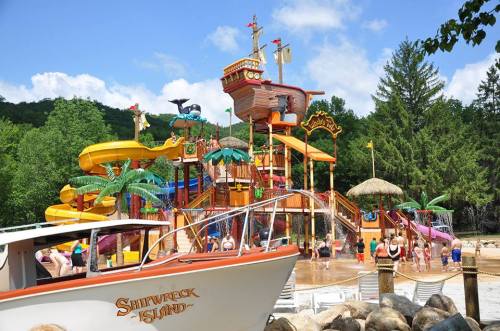 Colorful water park with slides and a pirate ship, surrounded by trees and people enjoying the water.
