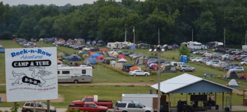 Aerial view of a large camping area with numerous tents and RVs, featuring a sign for Rock-n-Row Camp & Tube.
