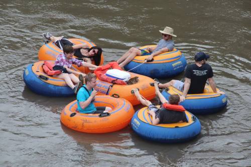 A group of six people relax on colorful inner tubes in a river, enjoying a sunny day outdoors.