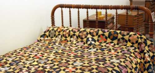 A wooden bed frame with a colorful quilt featuring a geometric pattern of triangles and squares.