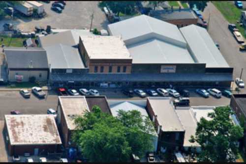 Aerial view of a small town with several buildings and parked cars along the street. Green trees are visible nearby.