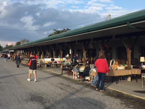A bustling outdoor market with people browsing tables filled with various items under a covered walkway.