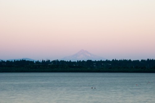 A serene lake at dusk with a distant mountain silhouette against a pastel sky.