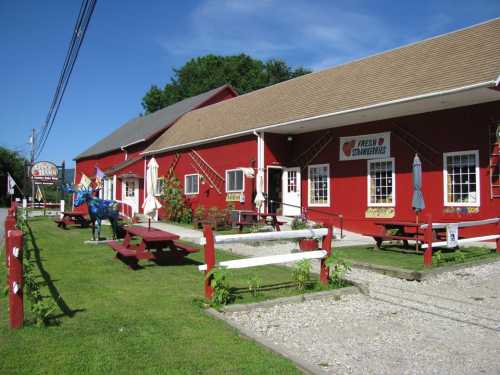 A red barn-style building with picnic tables outside, surrounded by green grass and blue skies.