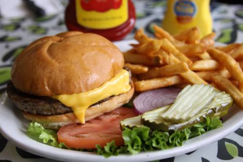 A cheeseburger with lettuce, tomato, pickles, and fries on a plate, with ketchup and mustard in the background.