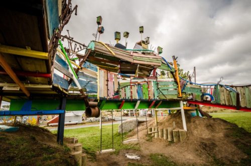 Colorful, whimsical playground structure with various shapes and textures, set against a cloudy sky.