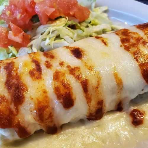 A close-up of a cheesy burrito with a golden-brown crust, served with lettuce and diced tomatoes on the side.