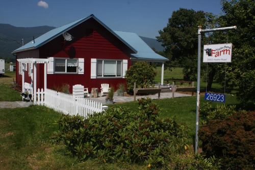 A red farmhouse with a blue roof, white picket fence, and sign for "Maple Tree Farm" in a scenic rural setting.