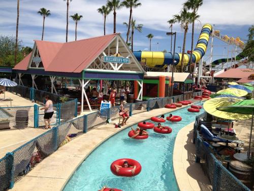 A water park scene with a lazy river, colorful tubes, and palm trees, featuring people relaxing and enjoying the sun.