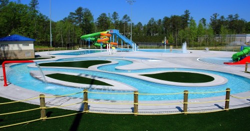 A vibrant water park featuring slides, a lazy river, and splash areas surrounded by green trees and blue skies.