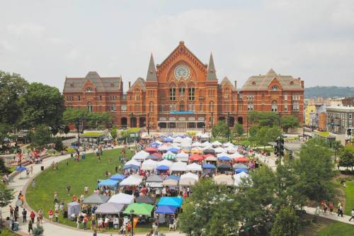 Aerial view of a vibrant outdoor market with colorful tents in front of a historic red brick building.