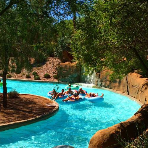 A group of people floating on inner tubes in a winding, turquoise waterway surrounded by trees and rocks.