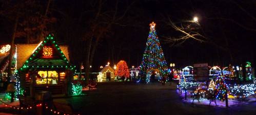 A festive scene at night featuring a large decorated Christmas tree and colorful lights illuminating a park.