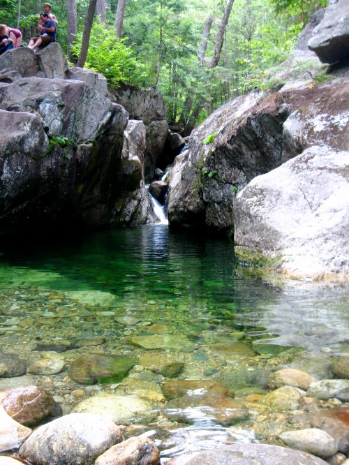 A serene natural pool surrounded by rocks and trees, with a small waterfall in the background.