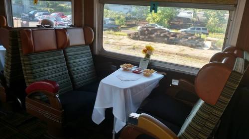 A cozy train dining area with two seats, a table set with snacks, and a view of the outdoors through the window.