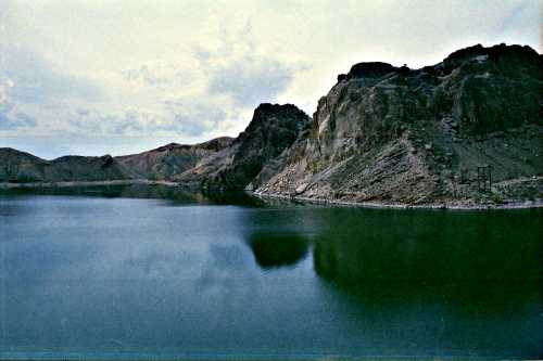 A serene lake surrounded by rocky hills under a cloudy sky, with reflections on the water's surface.