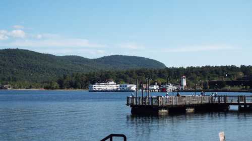 A scenic view of a lake with a dock, mountains in the background, and a boat near the shore under a clear blue sky.