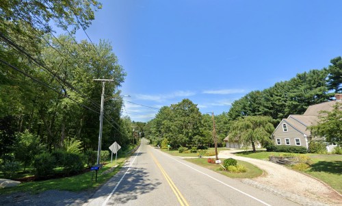 A quiet road lined with trees and houses under a clear blue sky.