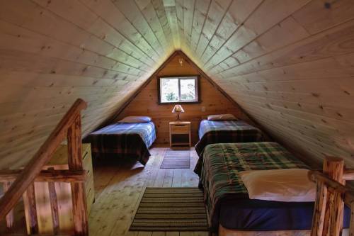 Cozy attic bedroom with two beds, wooden walls, and a small window letting in natural light.