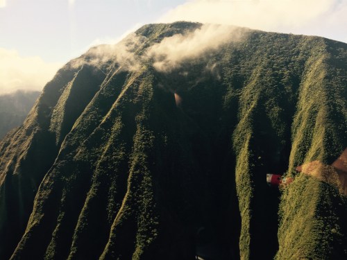 Lush green mountain slopes with clouds gently resting on the peaks under a clear blue sky.