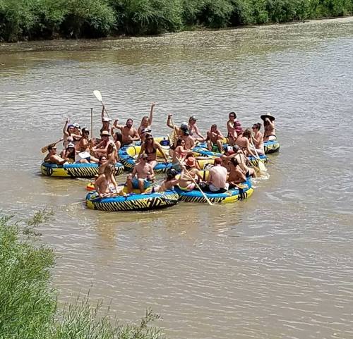 A group of people in inflatable rafts enjoying a sunny day on a river, some paddling and others cheering.