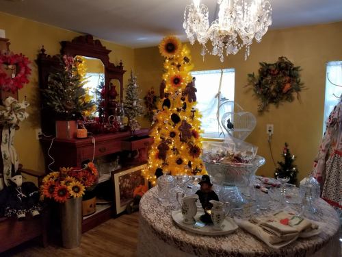 Cozy room decorated with sunflowers, a chandelier, and festive trees, featuring vintage furniture and holiday decor.