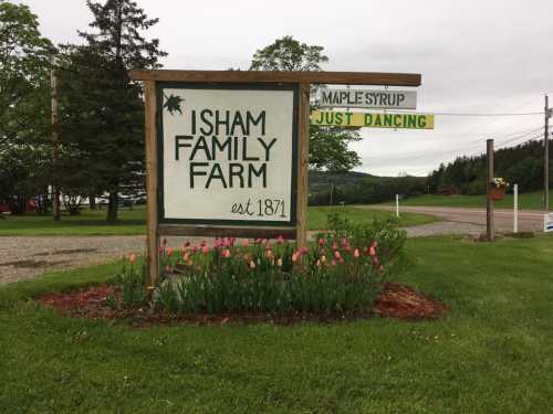 Sign for Isham Family Farm, est. 1871, with tulips in front and nearby signs for maple syrup and dancing.