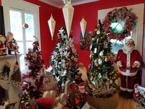 A cozy room decorated for Christmas, featuring multiple trees, festive ornaments, and a Santa figure.