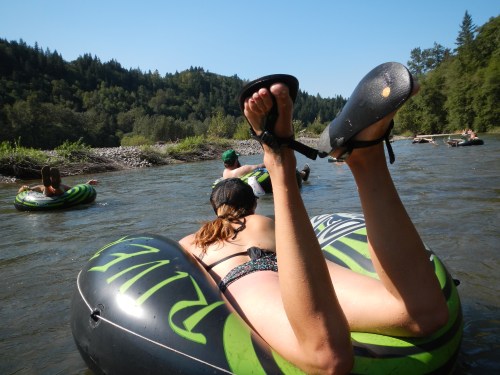 People floating on inner tubes in a river, surrounded by trees and a clear blue sky.