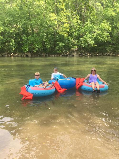 Three people relax on colorful inner tubes in a calm river, surrounded by lush green trees.