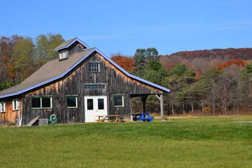 A rustic wooden building with a blue roof, surrounded by green grass and autumn-colored trees under a clear blue sky.