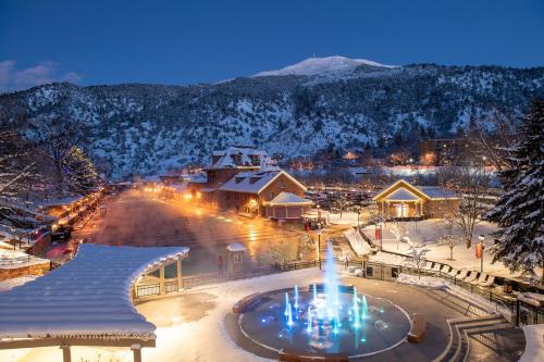 A snowy landscape at dusk featuring a fountain with colorful lights, surrounded by charming buildings and mountains.