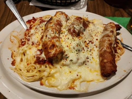 A plate of spaghetti topped with melted cheese and three crispy chicken tenders, garnished with herbs and spices.