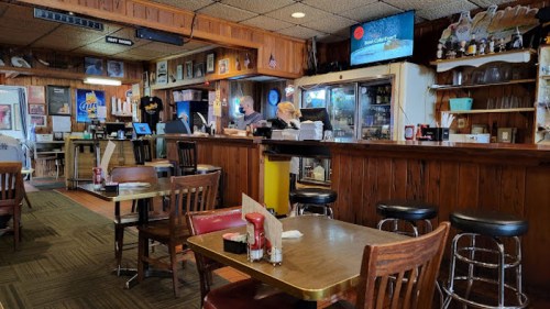 A cozy restaurant interior with wooden decor, tables, and a bar area where staff are serving customers.
