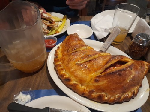 A large calzone on a plate, accompanied by a pitcher of beverage and a side of dipping sauce.