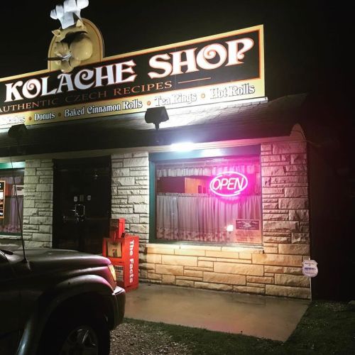 A brightly lit Kolache Shop at night, featuring a neon "OPEN" sign and a welcoming storefront.