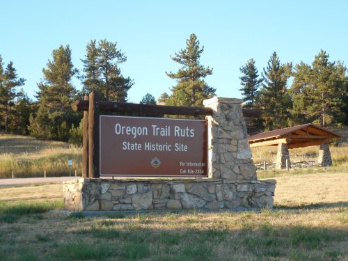 Sign for Oregon Trail Ruts State Historic Site, featuring stone structure and surrounding trees in a grassy area.