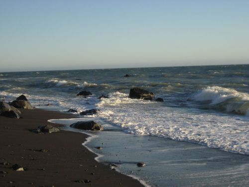 Waves gently crash on a rocky beach under a clear sky, with the ocean stretching into the horizon.