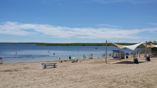 A sandy beach with people enjoying the water, umbrellas, and a clear blue sky in the background.