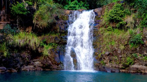 A serene waterfall cascading over rocky cliffs into a tranquil pool, surrounded by lush greenery.